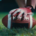 Close-up of a football player’s hand in gloves gripping a football before the snap during a night game